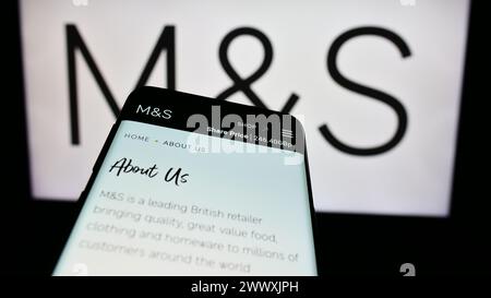 Smartphone with webpage of British retail company Marks and Spencer Group plc in front of business logo. Focus on top-left of phone display. Stock Photo