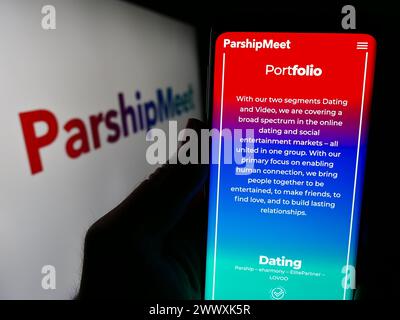 Person holding cellphone with webpage of German online dating company ParshipMeet Holding GmbH in front of logo. Focus on center of phone display. Stock Photo