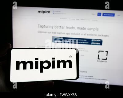 Person holding smartphone with logo of French real estate conference MIPIM in front of website. Focus on phone display. Stock Photo