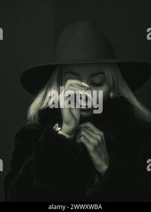 Monochrome image of a pensive blonde woman in a hat, her face partly obscured by her hand Stock Photo