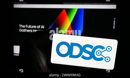 Person holding smartphone with logo of annual event Open Data Science Conference (ODSC) in front of website. Focus on phone display. Stock Photo