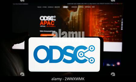 Person holding cellphone with logo of annual event Open Data Science Conference (ODSC) in front of webpage. Focus on phone display. Stock Photo
