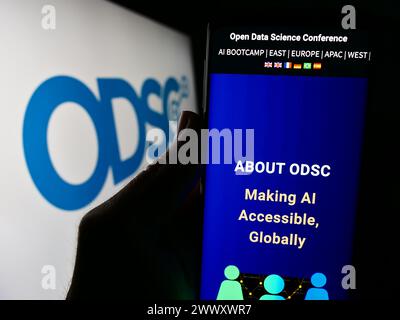 Person holding cellphone with webpage of annual event Open Data Science Conference (ODSC) in front of logo. Focus on center of phone display. Stock Photo