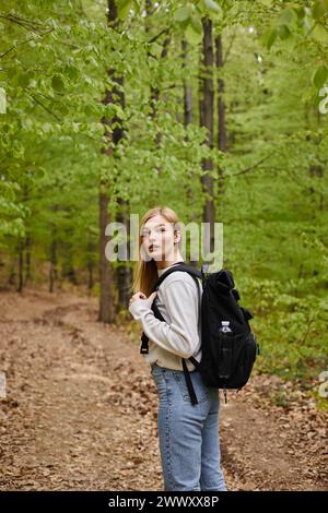 Side view shot of blond pretty woman traveler with backpack looking for direction walking in forest Stock Photo