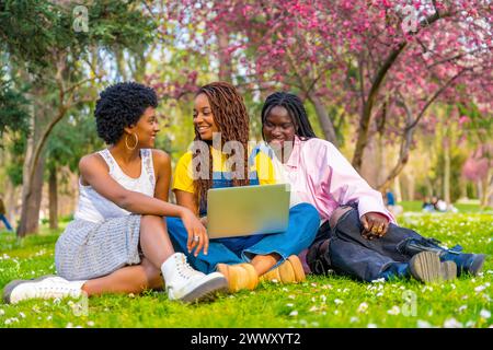 Three beauty young female african students using laptop sitting on the grass of the campus Stock Photo