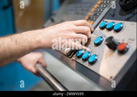 Worker pressing buttons on CNC machine control board in factory. High quality photography. Stock Photo