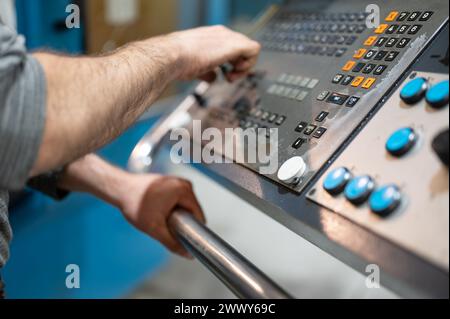 Worker pressing buttons on CNC machine control board in factory. High quality photography. Stock Photo