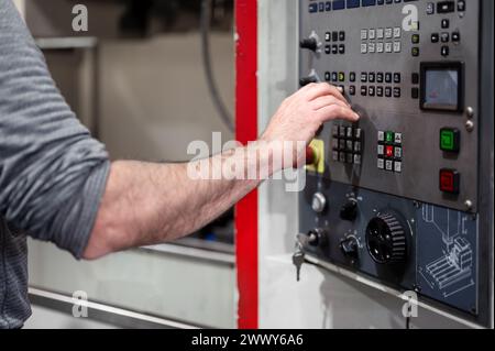 Worker pressing buttons on CNC machine control board in factory. High quality photography. Stock Photo