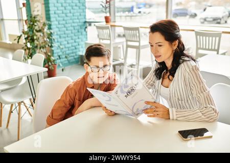 beautiful mother in casual attire looking at menu in cafe with her inclusive son with Down syndrome Stock Photo