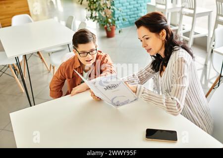 beautiful mother in casual attire looking at menu in cafe with her inclusive son with Down syndrome Stock Photo
