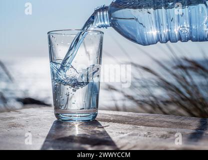 Pouring water into a glass from plastic bottle. Nature background. Stock Photo