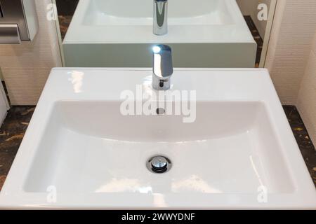 A white square bathroom sink with a faucet is positioned on top of a stonecounter Stock Photo