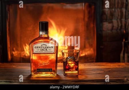 Kyiv, Ukraine – March 25, 2021. Bottle of Gentleman Jack Daniels whiskey with a glass of whiskey on an old wooden table in front of a burning fireplac Stock Photo