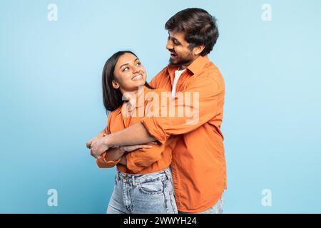 Portrait of loving indian couple embracing against blue backdrop Stock Photo