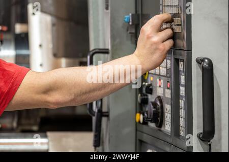 Worker pressing buttons on CNC machine control board in factory. High quality photography. Stock Photo