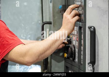 Worker pressing buttons on CNC machine control board in factory. High quality photography. Stock Photo