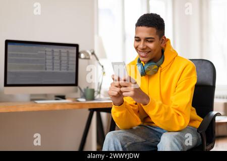 Smiling young man using smartphone at desk Stock Photo