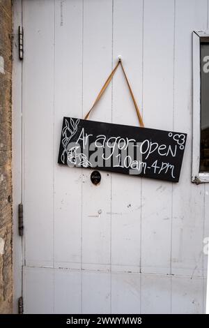 Wooden decorative sign in Welsh and English showing  the opening times for a shop in Wales. Bilingual. Wales. Stock Photo