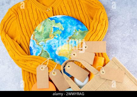 The sweater sleeves yellow holding in the embrace of the planet with an eco bag and tags. Responsible consumption. Creative concept buy less Stock Photo