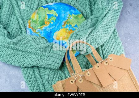 The sweater sleeves holding the tags in the embrace of the planet with an eco bag. Responsible consumption. Creative concept buy less Stock Photo