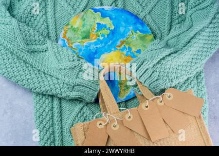 The sweater sleeves holding the tags in the embrace of the planet with an eco bag. Responsible consumption. Creative concept buy less Stock Photo