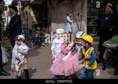 Several children are seen dressed in costumes during the Purim celebrations. A young girl wears a pink princess dress, while  the boys are dressed as an astronaut, a construction worker, and a doctor. Ultra-Orthodox Jews Celebrate Purim in Bnei Brak, Israel. The holiday commemorates the salvation of the Jews in ancient Persia from a plot to annihilate them. A joyous holiday, it is celebrated by both secular and nonsecular Jews, most notably by dressing up in costumes and drinking, according to the Talmud, “until they cannot distinguish between ‘cursed is Haman’ and ‘blessed is Mordechai.' Stock Photo