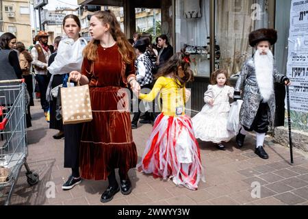 Bnei Brak, Israel. 24th Mar, 2024. Children walk along the main street dressed in costumes; a boy, dressed as a Rabbi with a long white beard, holds the hand of a young girl dressed as Queen Esther during the Purim celebrations. Ultra-Orthodox Jews Celebrate Purim in Bnei Brak, Israel. The holiday commemorates the salvation of the Jews in ancient Persia from a plot to annihilate them. A joyous holiday, it is celebrated by both secular and nonsecular Jews, most notably by dressing up in costumes and drinking, according to the Talmud, 'until they cannot distinguish between ''˜cursed is Haman'' Stock Photo