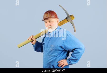 Serious miner worker in uniform with pickaxe. Construction and building works. Bearded man in coveralls and hard hat with pick axe. Craftsman working Stock Photo