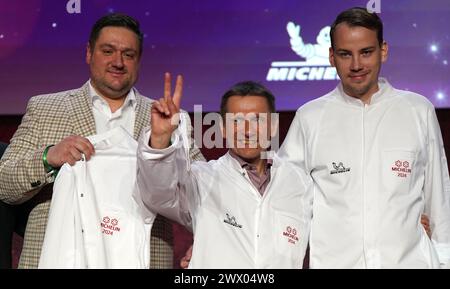 26 March 2024, Hamburg: Maximilian Waibel (l), Sous Chef of the two-star restaurant "Komu" in Munich, two-star chef Ulrich Heimann (M) from the restaurant "Pur" in Berchtesgaden and two-star chef Roland Pieber (r) from the restaurant "Seo Küchenhandwerk" in Langenargen stand on stage during the award ceremony for the Michelin Stars 2024 for German restaurants at the Chamber of Commerce. This year's "Guide Michelin" restaurant guide lists 340 restaurants that have earned one or more stars in recent months, including ten three-star restaurants. Restaurant " Photo: Marcus Brandt/dpa Stock Photo
