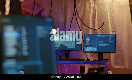 Empty abandoned underground warehouse with lines of code running on computer screen with malware that get past security systems. Monitors in hidden HQ showing scripts that can hack devices Stock Photo