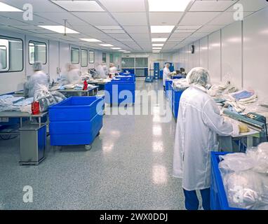 Workers are gowned up to work in clean rooms.  There are blue bins in the image. Stock Photo