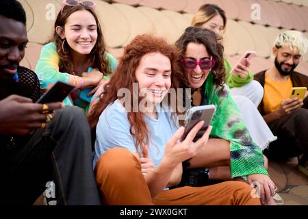 Side view large multiracial group young friends using cell phones outdoors. LGBT diverse community. Stock Photo