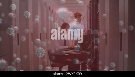 Image of virus cells over caucasian workers in server room. Global technology and digital interface concept digitally generated image. Stock Photo