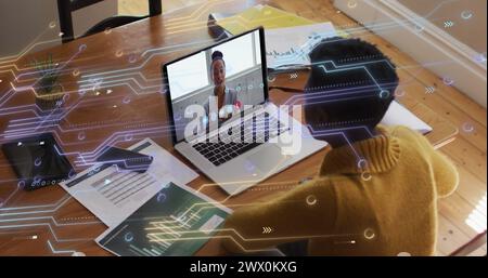 Image of microprocessor connections over african american woman having a image call on laptop. Global networking and business technology concept Stock Photo