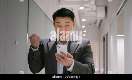 Happy surprised Asian mature man emotional winner male chinese korean businessman smiling entrepreneur winning business success celebrate amazing news Stock Photo