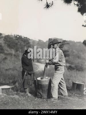 Taken at Camp John Hay Native Barrio, Baguio, Philippine Islands An Ifugao woman watches an American Soldier try his hand at pounding rice ca. 1931 Stock Photo