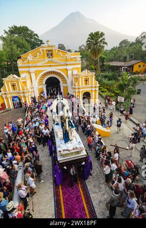 Antigua, Guatemala. 26th Mar, 2024. Catholic penitents carry the the Jesus of Nazareth processional float out from the Ermita de El Calvario with the Agua Volcano rising behind, March 26, 2024 in Antigua, Guatemala. The opulent processions, detailed alfombras and centuries-old traditions attract more than 1 million people to the ancient capital city. Credit: Richard Ellis/Richard Ellis/Alamy Live News Stock Photo