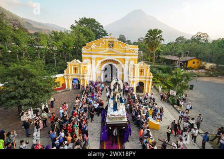 Antigua, Guatemala. 26th Mar, 2024. Catholic penitents carry the the Jesus of Nazareth processional float out from the Ermita de El Calvario with the Agua Volcano rising behind, March 26, 2024 in Antigua, Guatemala. The opulent processions, detailed alfombras and centuries-old traditions attract more than 1 million people to the ancient capital city. Credit: Richard Ellis/Richard Ellis/Alamy Live News Stock Photo