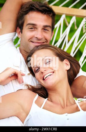 Portrait, happy couple and relax on hammock in nature, love and vacation in summer on tropical island. Young man, woman and face in marriage at beach Stock Photo