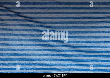 Front view of wrinkled tarp with blue and white stripes. Abstract high resolution full frame textured background. Stock Photo