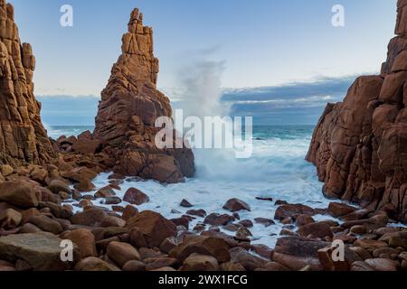 A large wave crashing against a tall sea stack along a rocky coastline at Cape Woolamai on Phillip Island in Victoria, Australia Stock Photo