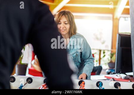 Young woman engaging in foosball table game, displaying a focused demeanor, indoor leisure setting - Engaged, relaxed posture and attentive gaze highl Stock Photo