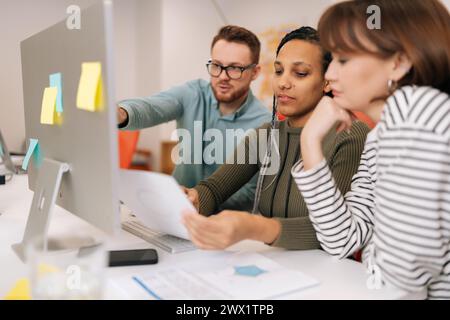 Skilled male CEO mentor or executive manager boss teaching diverse internes, explaining work pointing at computer screen. Team leader supervisor Stock Photo
