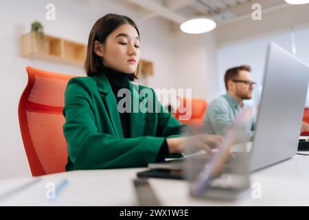 Low-angle view of serious female programmer typing program code on laptop keyboard in coworking. Focused young copywriter writing text working in big Stock Photo