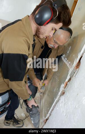 men using hammer drill to remove plaster from wall Stock Photo