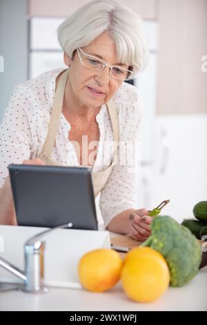 smiling senior woman in apron using digital tablet in kitchen Stock Photo