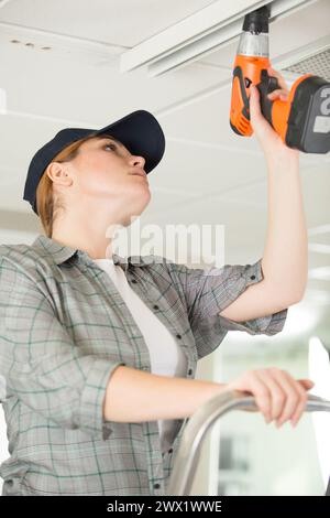 woman using cordless drill on ceiling Stock Photo