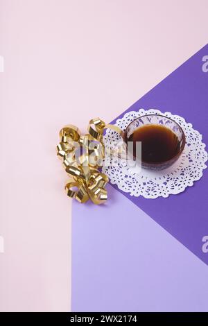 a violet cube made with colored paper to create a 3D optical illusion. On top is a gold Gift ribbon curled near a vintage pink coffee cup with a white Stock Photo