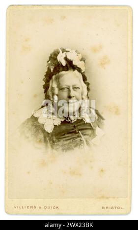 Original Victorian Carte de Visite (visiting card or CDV) portrait of older, smiling, kind looking middle aged Victorian lady, Victorian woman, in black clothes and wearing a bonnet trimmed with lace, long curled grey hair, studio of Villiers and Quick, Bristol, U.K. Circa 1870's Stock Photo