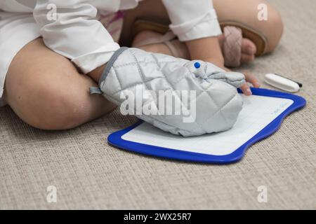 Close up of kid sitting at the classroom, playing. The kid is drawing on an whiteboard with a sharpie while wearing an oven mitt Stock Photo